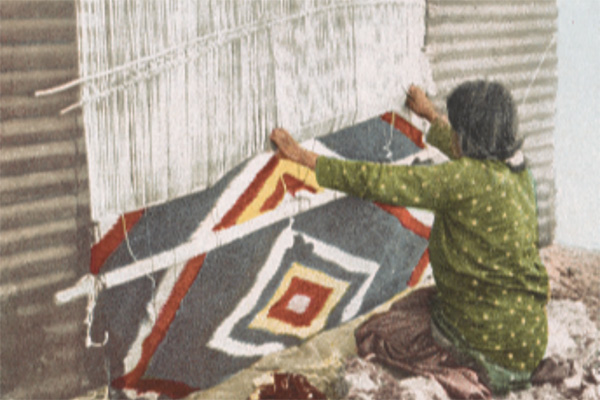 Women weaves traditional Navajo blanket hanging on a wall.