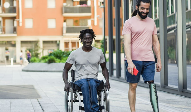 A man in a wheelchair accompanied by another man with a prosthetic leg.