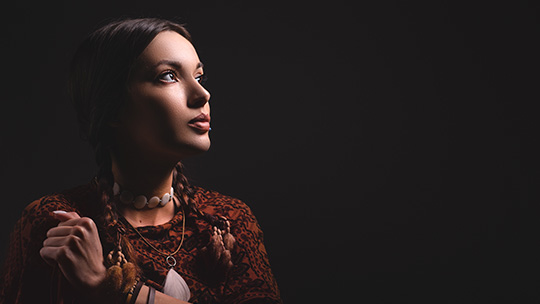 A Native American woman in traditional clothing stares into the distance.