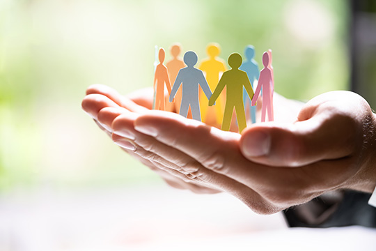 Colorful Silhouettes of people holding hands are held up by a person’s nurturing hands.