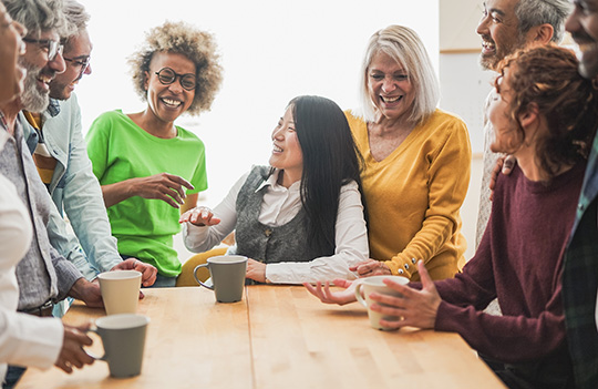 A group of women and men of all ages sitting and standing around a table.