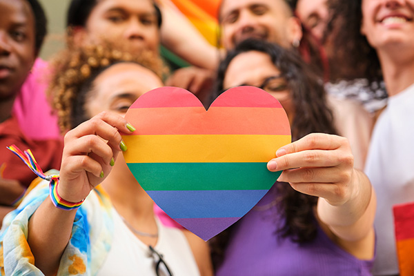 Two people holding a paper cut-out shaped like a heart with a crowd behind them.