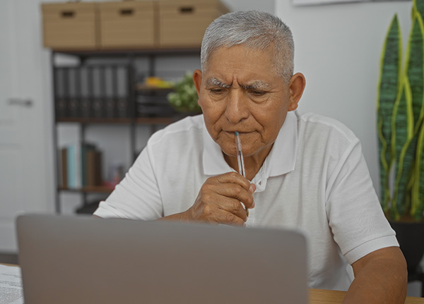 An older Hispanic man looking at his laptop computer. 