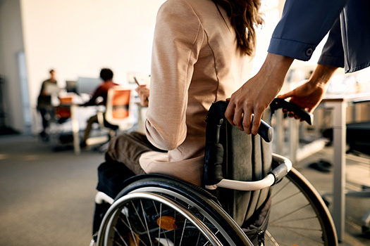 Close-up of colleague pushing businesswoman in wheelchair while arriving in the office