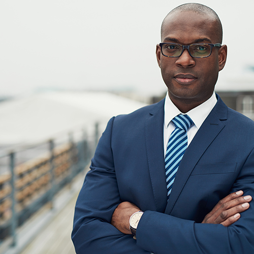 A Black man in a suit standing with his arm crossed