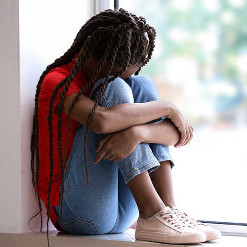 Sad girl sitting on windowsill