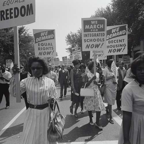 A group of people walking down a street holding protest signs