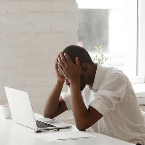 Black male sitting at table with his head in his hands