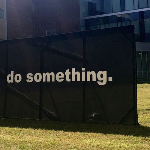 A large black scaffolded sign that reads White people. Do something