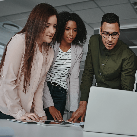 Two women and a man looking at a laptop in an office setting