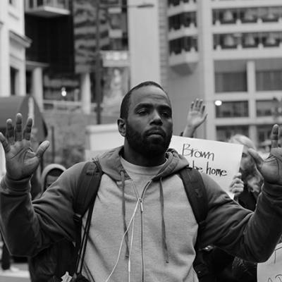 A young black man protesting with his hands up.