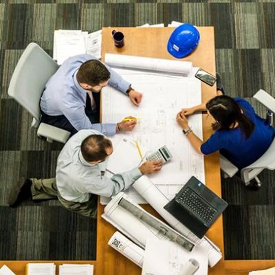 Overhead shot of 3 people sitting at a table collaborating on a project.