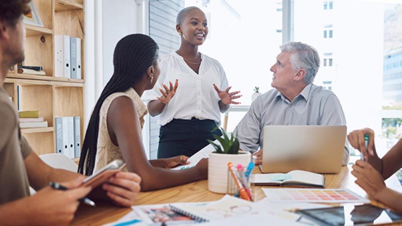 Image of a diverse team with an African American woman standing and speaking.