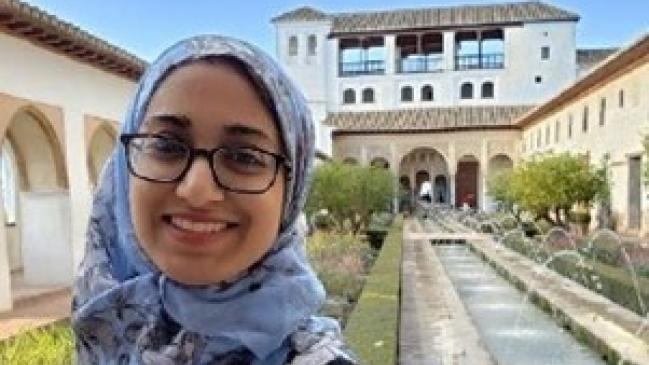 Photo of the author, Zulekha Sayyed, an Indian-American woman wearing glasses, a headscarf, and a flower print dress. 